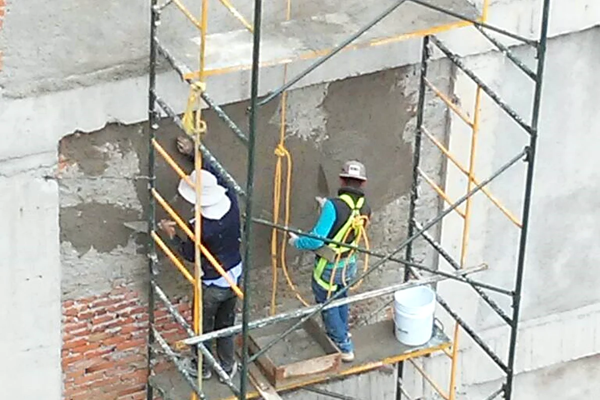 Trabajadores en andamio aplicando mortero sobre un muro de concreto