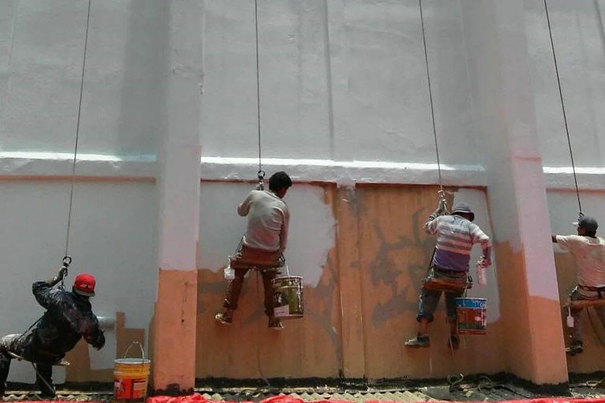 Pintores en rapel aplicando pintura en la fachada de un edificio